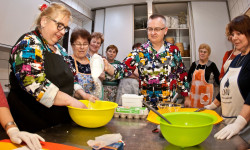 w kuchni przy stole kuchennym mężczyzna i kilka kobiet w fartuchach jedna z nich miesza w misce  