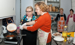 w kuchni przy kuchence dwie kobiety w fartuchach jedna z nich przelewa z patelni płyn do drugiego garnka  