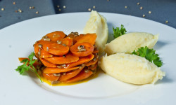 biały talerz na talerzy marchewka pokrojona w plastry oblana ciemnym sosem obok 3 gałki ziemniaków udekorowane pietruszka 