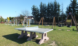 Zdjęcie przedstawia huśtawki oraz stół do ping-ponga oraz siłownie zewnętrzną