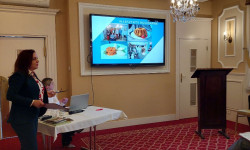 Konferencja LGD. Hrubieszów. W sali kobieta przemawia do zebranych osób. Za nią ekran z prezentacją. 