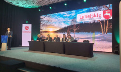 Przy stole na scenie siedzi 5 osób podpisują dokumenty. Za nimi na ekranie zimowy widok i napis lubelskie. 