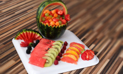 na białej tacy pokrojone owoce i arbuz wycięty w koszyczek w środku kawałki owoców