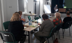 grupa ludzi przy stole i osoba prowadząca rozmawiają