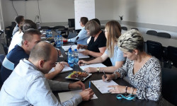 grupa ludzi przy stole i osoba prowadząca rozmawiają