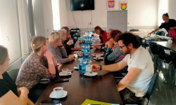 grupa uczestników spotkania siedzących przy stole słuchają wypowiedzi osoby prowadzącej